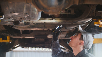Mechanic is checking the bottom of car in garage automobile service, close up