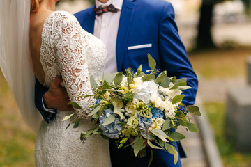 Groom holds gorgeous wedding bouquet while he hugs bride's waist