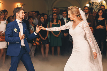 Handsome groom in blue suit takes bride's hand while he dances w