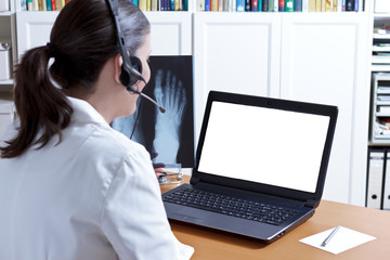 Female doctor in her surgery office with headphones in front of her laptop, an x-ray of a foot in...