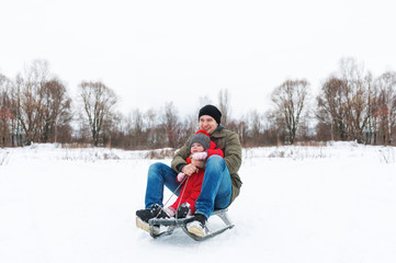 Fototapeta na wymiar Young man with the little daughter sitting on sledge in snow