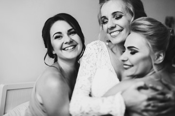 Pretty bridesmaids hug gorgeous bride tender sitting on bed