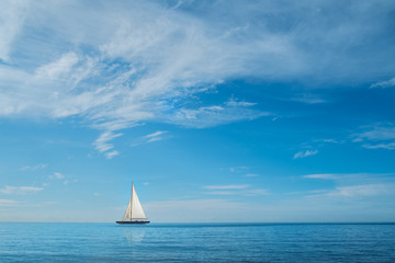 Obraz premium Sail boat on horizon at sea with blue sky and clouds
