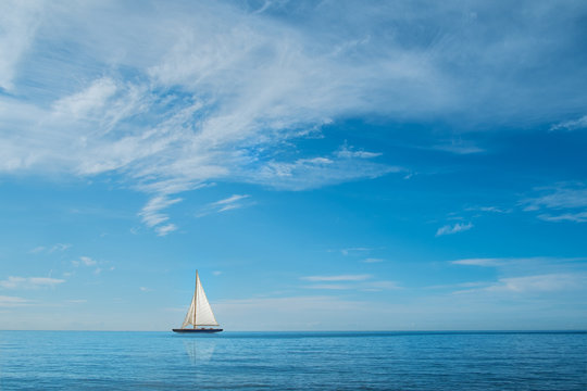 Sail boat on horizon at sea with blue sky and clouds