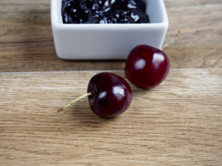 Cherry jam with two cherries on wood background