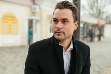 Naklejka premium the man in a black coat sits at a stop. His eye is turned somewhere and it seems that he has seen someone. He has on a face a faint smile and very intriguing look.