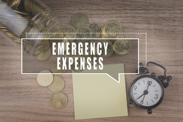 Coins spilling out of a glass jar on wooden background with EMERGENCY EXPENSES text . Financial Concept