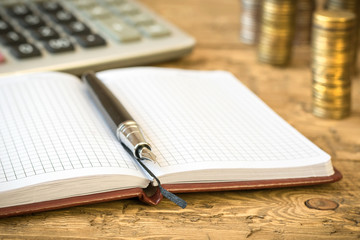 Fountain pen,calculator, coins and notebook on a wooden table.