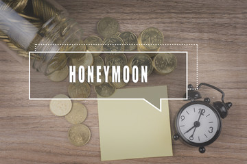 Coins spilling out of a glass jar on wooden background with HONEYMOON text . Financial Concept