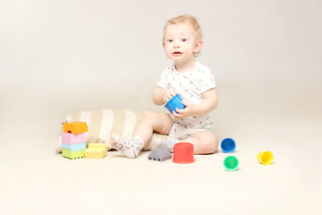 Studio shot of surprised adorable baby boy sitting on the floor and playing with some toys.