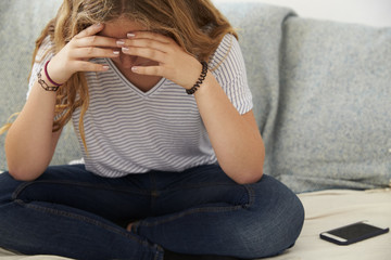 Fototapeta premium Depressed teenage girl sitting alone at home, head in hands