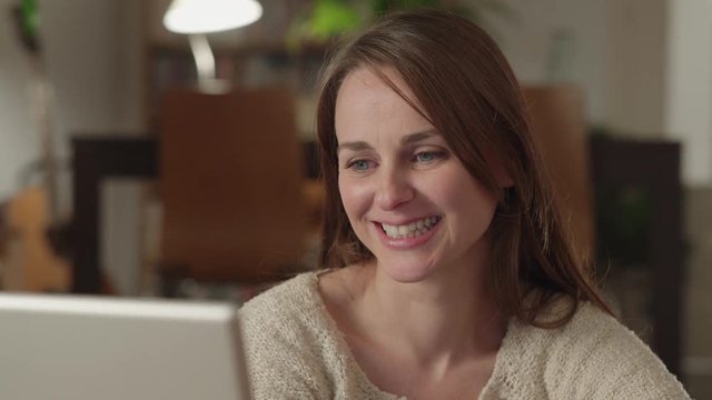Young woman watches videos on internet in her laptop at home. She smiles and something surprised her.