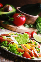 Salad with avocado, salmon, lettuce, onions and peppers on a pla