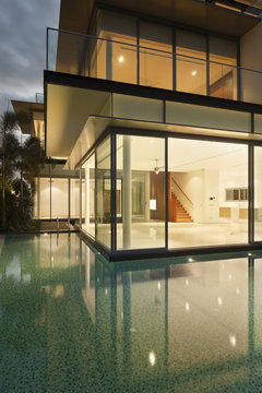 View into lit house with reflections in water of residential house 