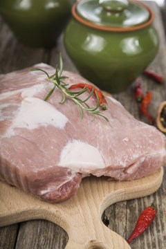 Raw pork ,ceramic pots, rosemary and spices on a wooden board on