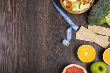 Food for diet and measuring tape on a dark wooden table.