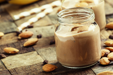 Chocolate almond smoothie in glass jars, old wooden background,