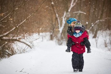 Fototapeta na wymiar Cute kid boy carrying his friend while walking in a winter park. Children playing and having fun.