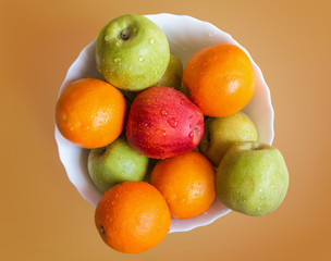 apples and orange on white dish, orange background top view