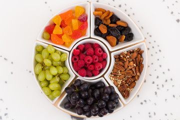 Round set of plates full of nuts, raspberries, sweets, grapes and dry fruit on the white background. Healthy snacks. Desserts for  coffee or tea. Assorted mix of pecans, berries and fruit.