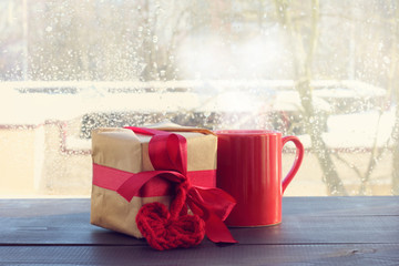 warming atmosphere of love/ gift with heart symbol and a hot drink on the background of the window