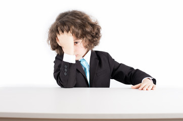 Little curly manager in a business suit sitting at his desk, his head in his hand looking sadly at the camera. White background.
