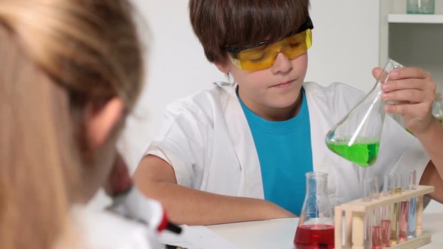 Elementary school chemistry class - kids experimenting, focus on background boy