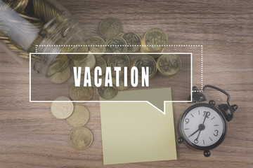 Coins spilling out of a glass jar on wooden background with VACATION text . Financial Concept