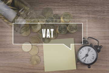 Coins spilling out of a glass jar on wooden background with VAT as VALUE ADDED TAX text . Financial Concept