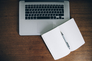 Laptop keyboard, pen, and a paper notebook on a wooden table background
