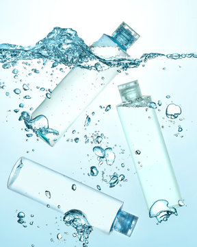 Three bottles of thermal water, cosmetic moisturizing lotion under the water. Big wave on the surface of water and many big and small bubbles in the water. Gradient blue background