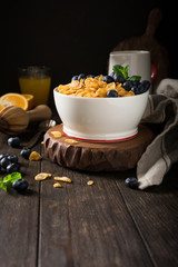 Healthy breakfast with corn flakes, berries and milk on old dark wooden background. Copy space.