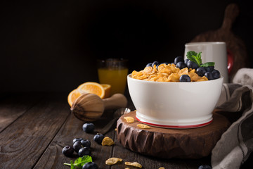 Healthy breakfast with corn flakes, berries and milk on old dark wooden background. Copy space.