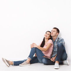 Happy young couple sitting on floor looking up while dreaming their new home and furnishing. Mock up.