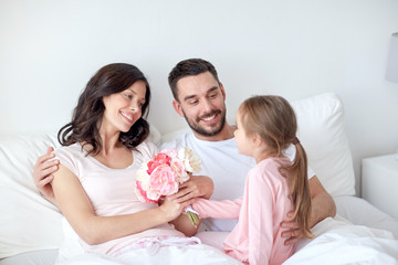 happy girl giving flowers to mother in bed at home