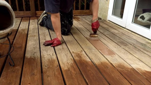 A deck balcony being oiled with a stain and protector by hand by brush.