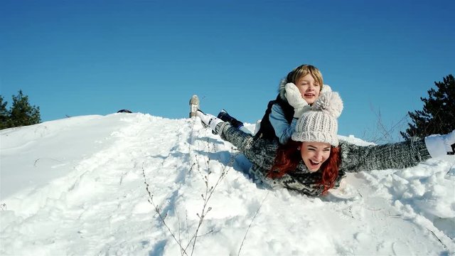 happy mother and son moves down on sled, family sleigh ride through the snow, sledding down the hills, fast descent on snowy slope in woods, fun winter holidays, winter
