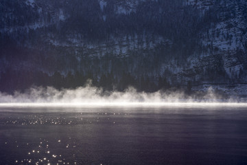 Morning Fog on the Mountain Lake with Snow Covered Shore. Winter Landscape.