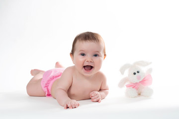 Little girl smiling with a toy rabbit lies on white background.