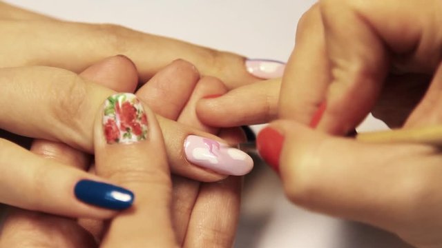 Beauty shop manicure session, woman hand painting colorful pattern on nail varnish, close up