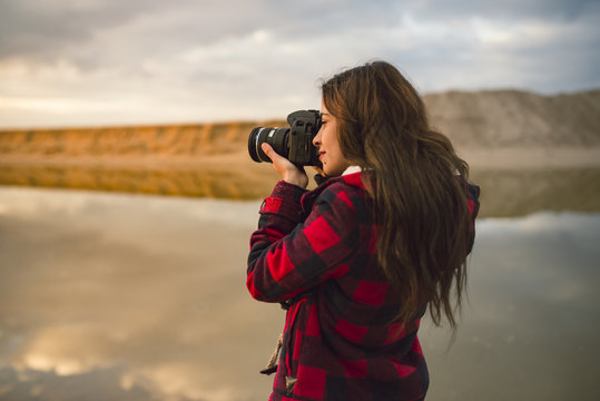 Young woman taking picture on the beach with camera at sunset