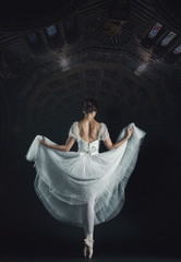 Portrait of the classical ballerina in white dress on black back