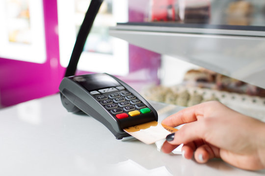 Female hand with silver bank card using the pos-terminal for payment.