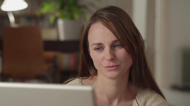 Young woman watches videos on internet in her laptop at home. She watches very concentrated and serious. Dolly shot to the right.