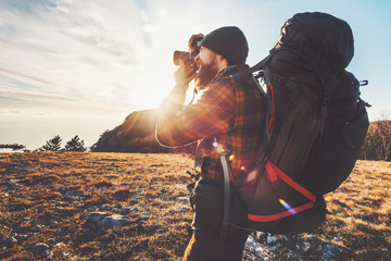 Man photographer with big backpack and camera taking photo of sunset mountains Travel Lifestyle hobby concept adventure active vacations outdoor - obrazy, fototapety, plakaty