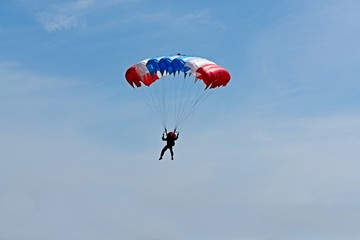 parachute jumping, skydiver descends by parachute flying on the blue sky background.