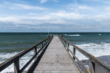 pier with stormy sea under blue sky with scattered clouds