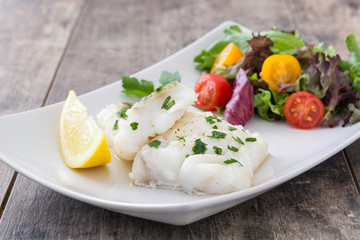 Fried cod fillet and salad in plate on wooden background
