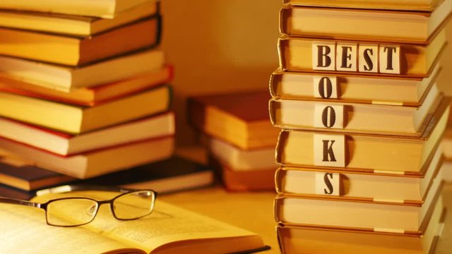 On a pile of books appears phrase BEST BOOKS. Open book with glasses on background of stacks of books. Stop motion