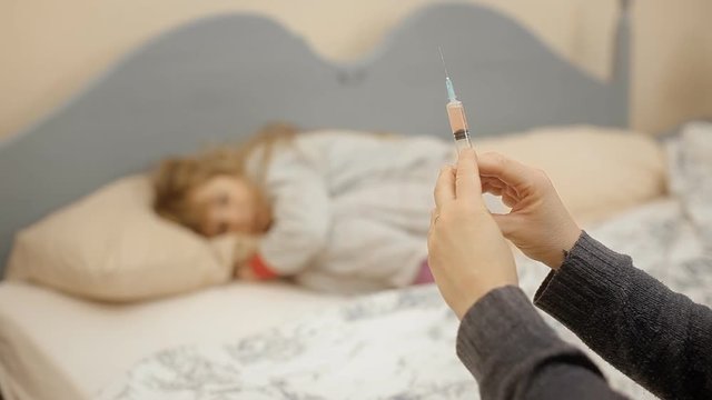 A little girl in her bed (blurred) looking at a syringe (on focus). She is afraid but not moving at all.
